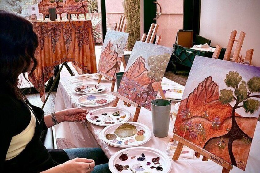 An artist painting landscapes on easels with palettes and brushes on a table. 1