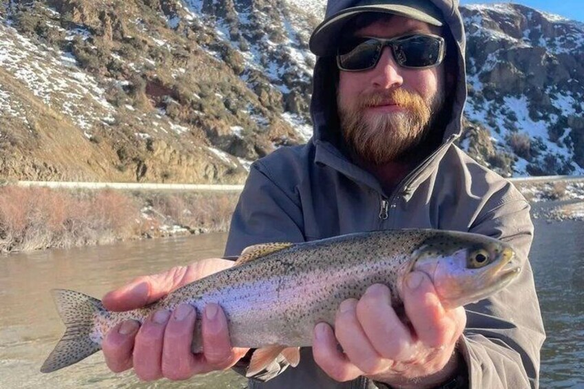 A person holding a fish near a river with mountains in the background. 5