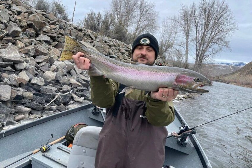 A person holding a large fish on a boat near a rocky riverbank. 3