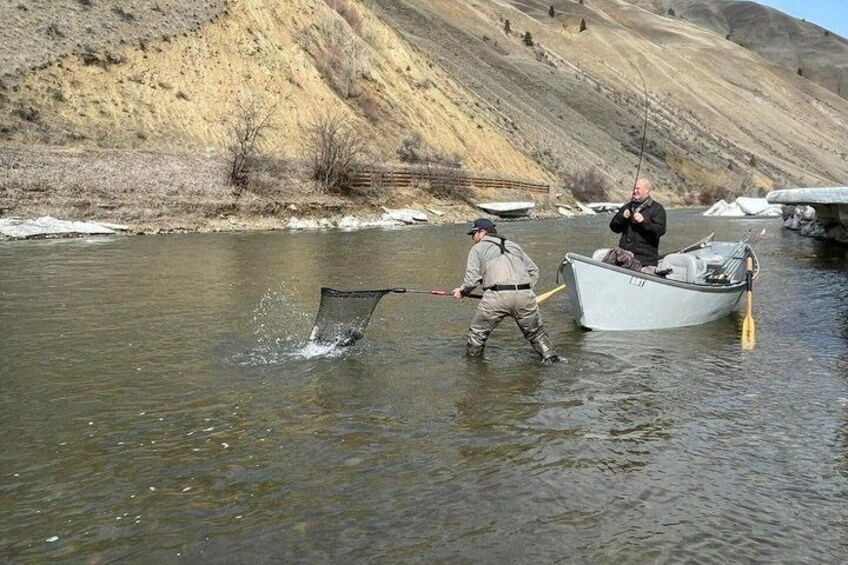 Two people fishing by a river with a boat and a net. 1