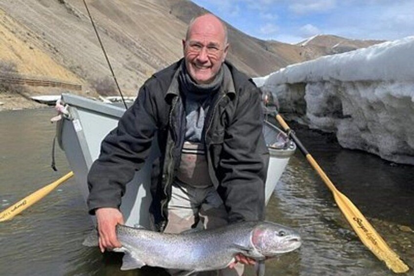 A person holding a fish in a river with ice in the background. 3