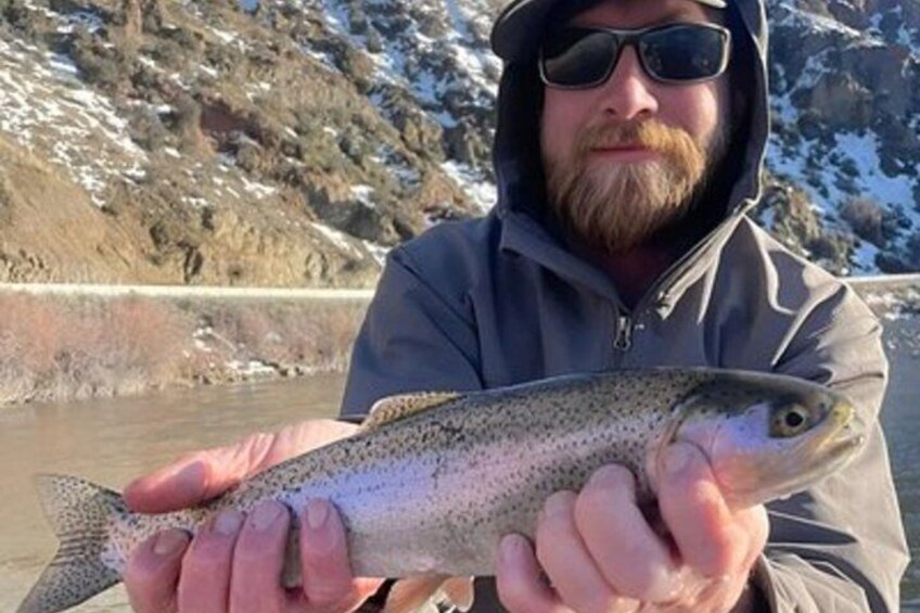 A person holding a fish by a river with rocky terrain in the background. 3