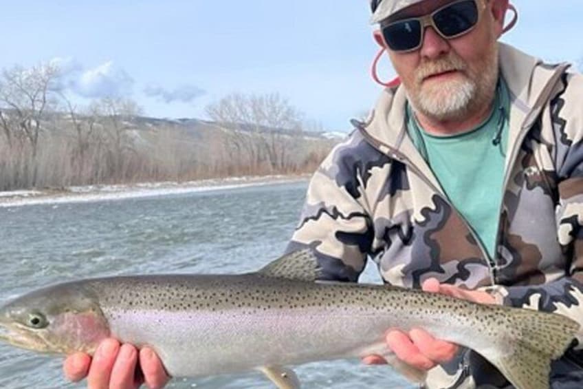 A person holding a large fish by a river. 5