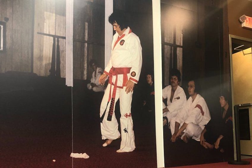 Una persona con uniforme blanco de artes marciales y cinturón rojo, de pie en una habitación con otras personas con atuendo similar. 2