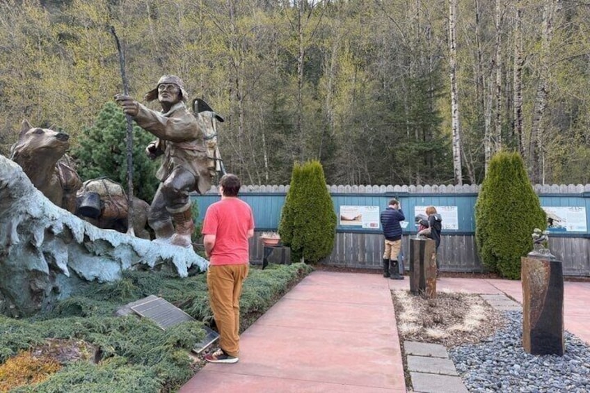 A statue of a man with a dog, a red pathway, and a wooden fence with informational signs. 1