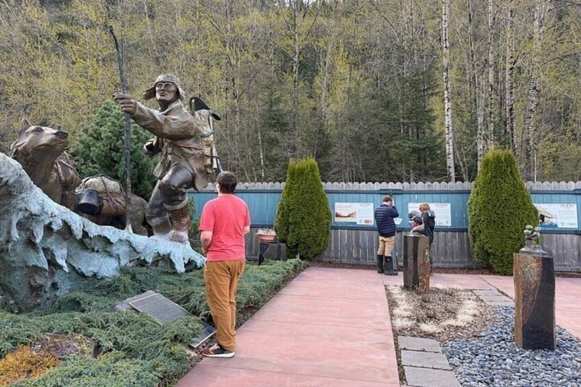 A statue of a man with a rifle, a bear, and a forested background. 1