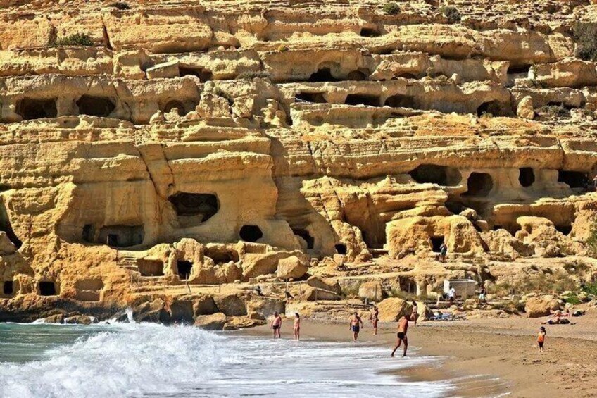 A rocky cliff with numerous caves and a beach with people. 5