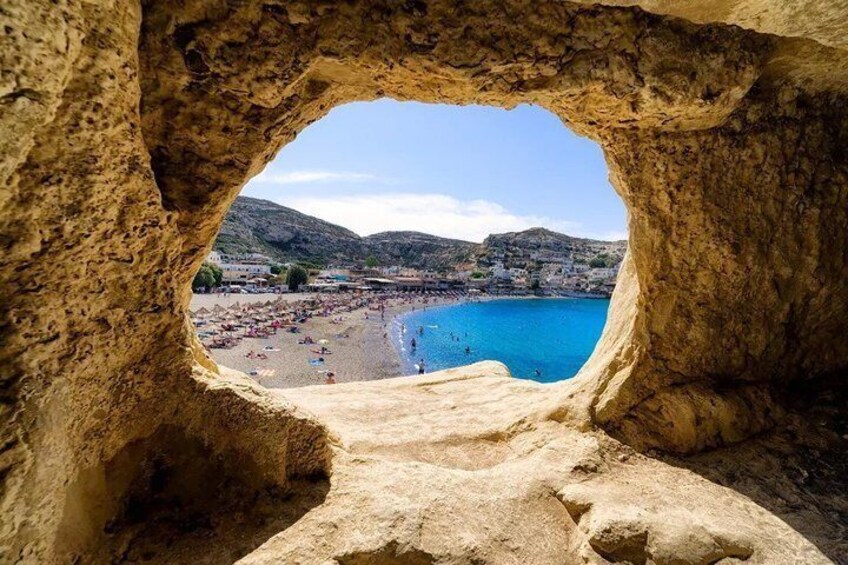 A view through a rock arch to a beach with people and a town in the background. 2