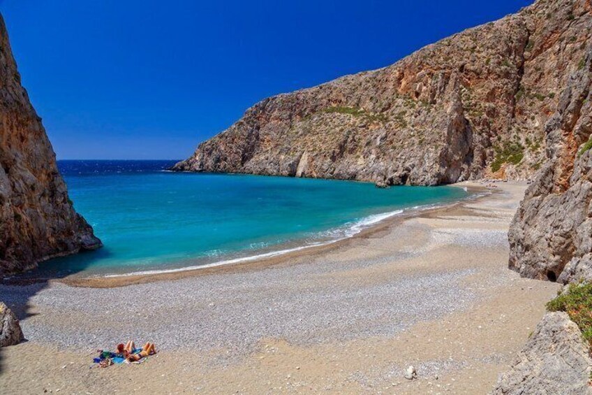 A beach with clear turquoise water, rocky cliffs, and a small group of people on the sand. 3