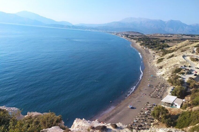 A coastal landscape with a beach, rocky outcrops, and distant mountains. 4
