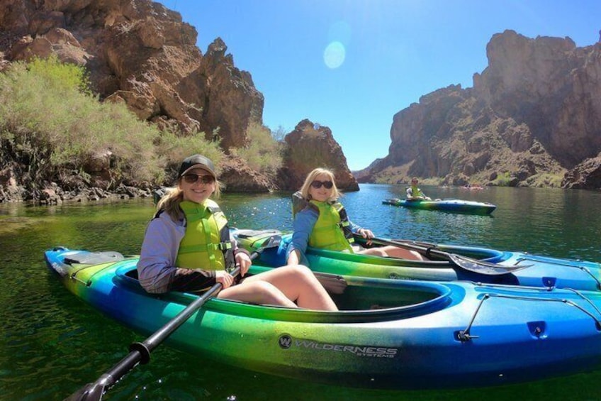 Two people in kayaks on a calm river surrounded by rocky cliffs. 4