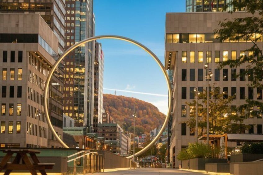 A cityscape with modern buildings, a circular structure, and a hill in the background. 2
