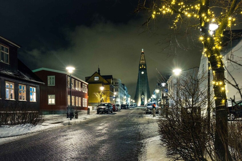 En snötäckt gata i mörkret, med byggnader, bilar och ett torn som är upplyst. 4