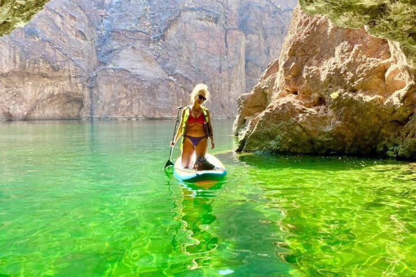 A person paddleboarding in clear water with rocky cliffs in the background. 5