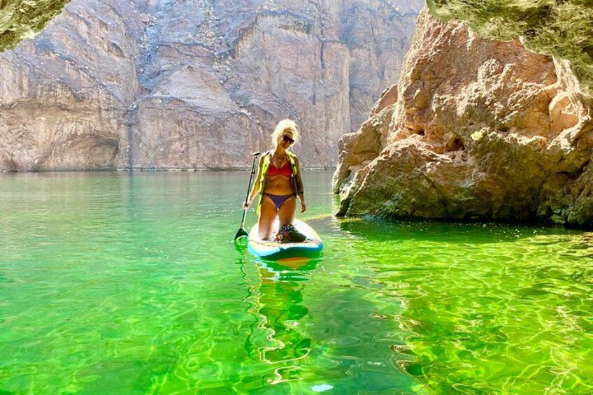 A person paddleboarding in clear green water with rocky cliffs in the background. 5