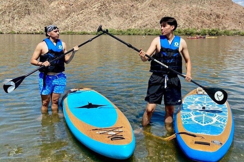 Two people standing on paddleboards in a body of water with a rocky landscape in the background. 2