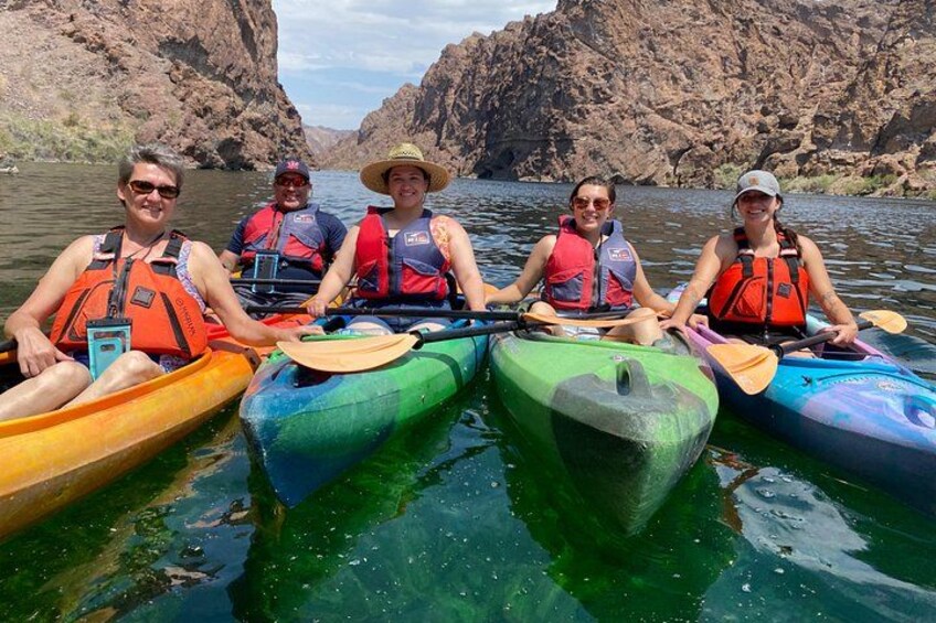 A group of people kayaking on a river surrounded by rocky cliffs. 1