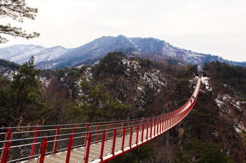 A red suspension bridge over a mountainous landscape. 3