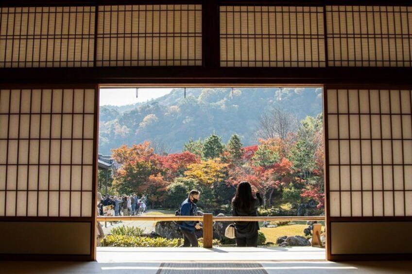 A traditional Japanese building with tatami mats and a view of a park with autumn foliage. 2