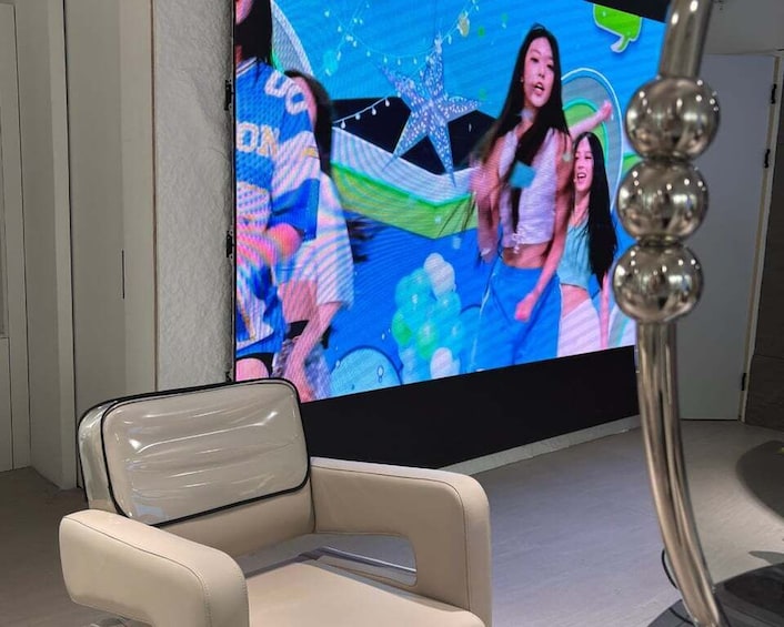 A modern interior with a large screen displaying a colorful image, a white chair, and a metallic sculpture. 1