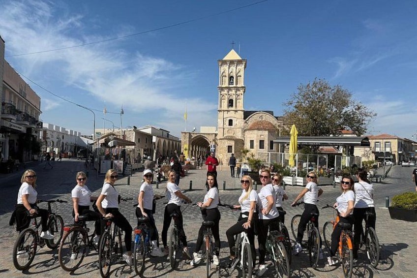 A group of people on bicycles in a town square with a historic building in the background. 1