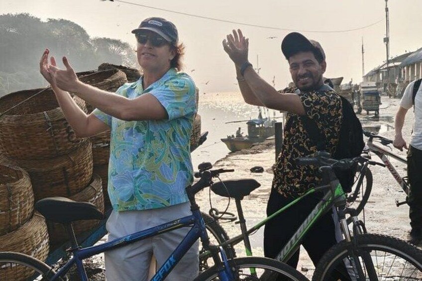 Two people standing by bicycles, a beach, and boats in the background. 5