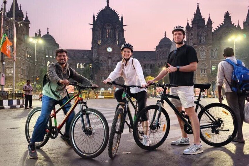 Three people on bicycles in front of a historic building with intricate architecture. 1