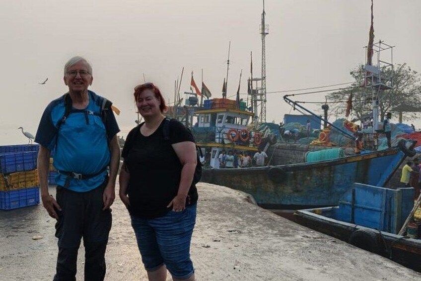Two people standing on a dock with fishing boats in the background. 3