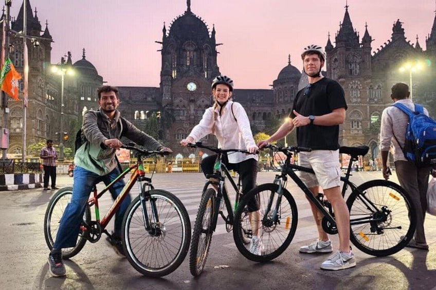 Three people on bicycles in front of a historic building with intricate architecture. 1