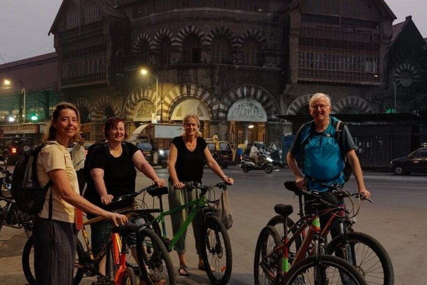 Four people with bicycles in front of a historic building with arched windows. 2