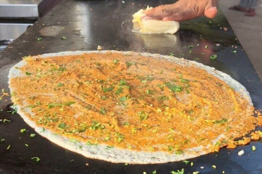 A person seasoning a large flatbread with spices and herbs on a black cooking surface. 4