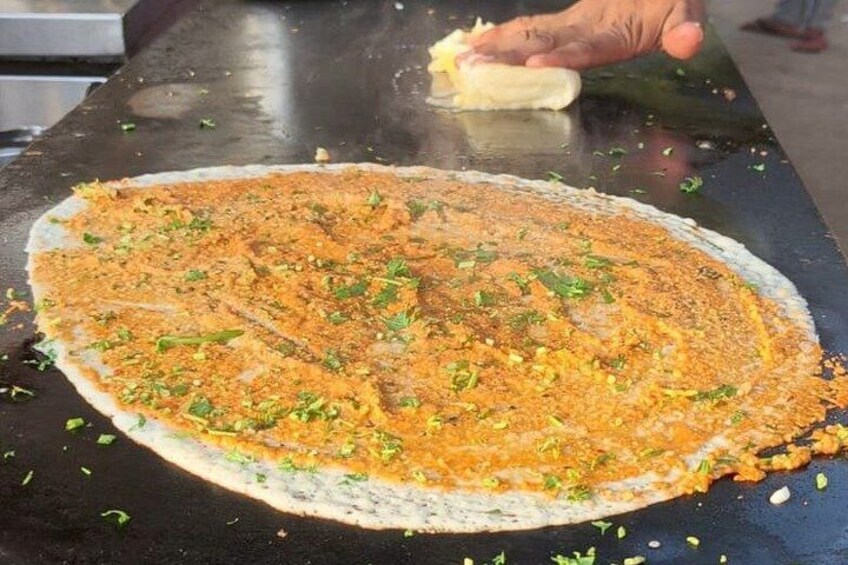 A flatbread being prepared on a hot surface with a hand sprinkling spices. 4