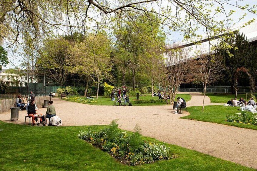 A park with people sitting on benches, a dirt path, and green grass. 4