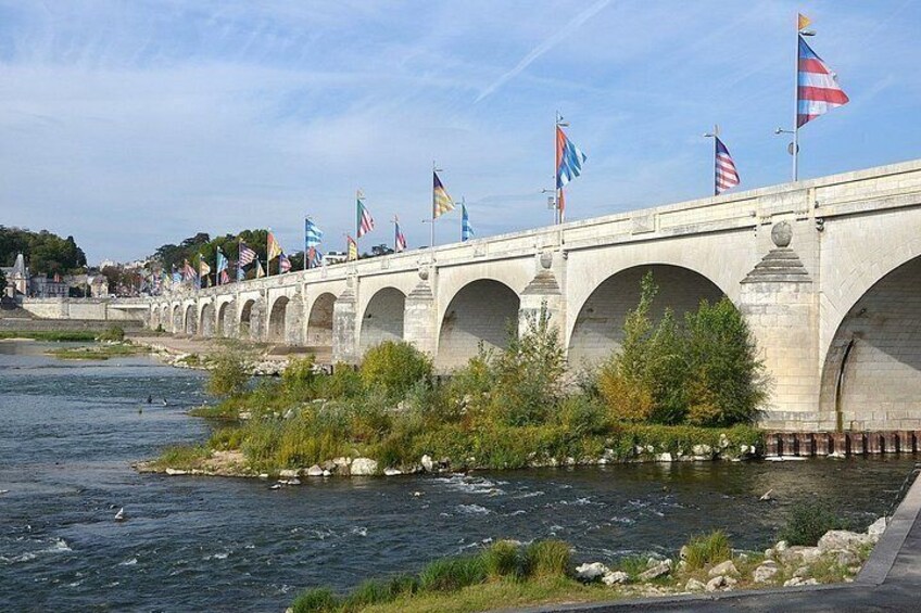 A stone bridge with multiple arches over a river, adorned with various flags. 2
