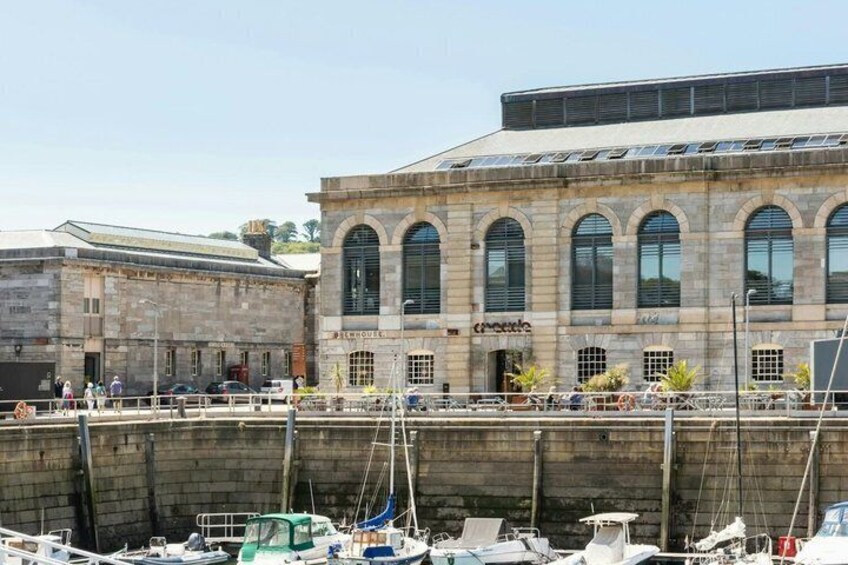 A historic building with arched windows and a sign that reads 'PIMOURGE.' Boats are docked in the foreground. 3