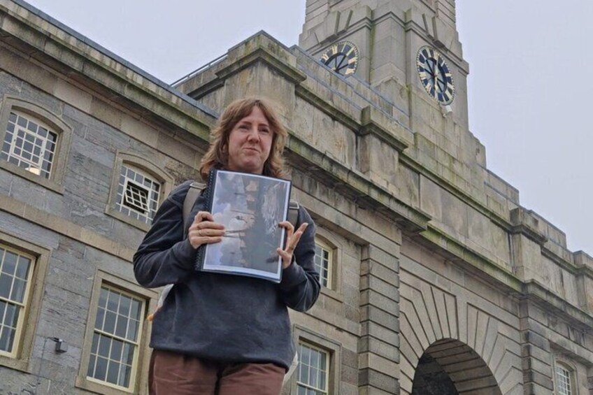 A person holding a book in front of a historic building with a clock tower. 2