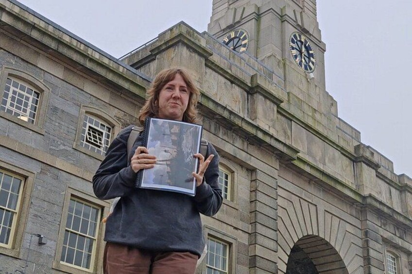 A person holding a book in front of a historic building with a clock tower. 3