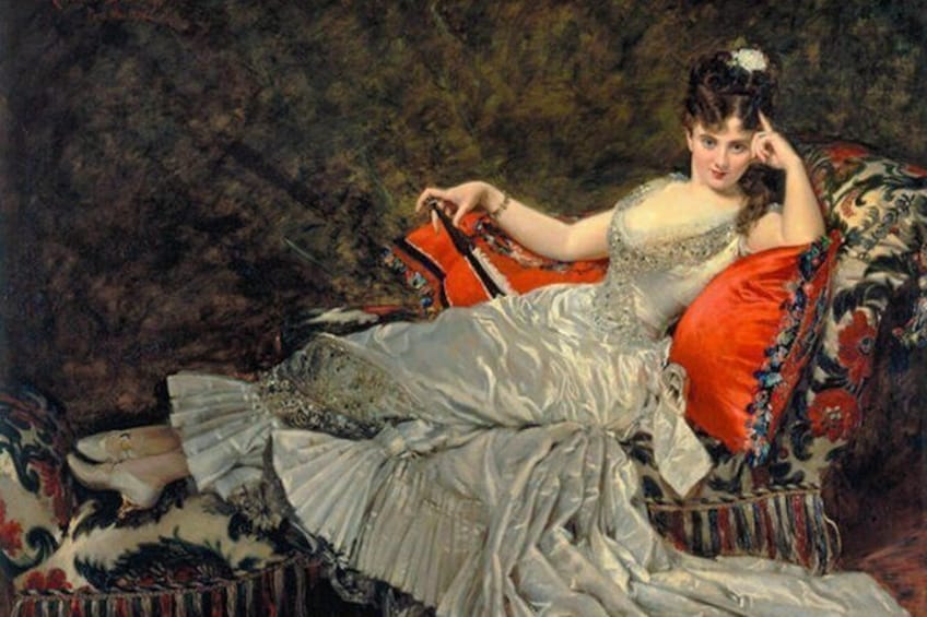 A person in a white dress sitting on a red and black patterned sofa with a floral arrangement on the table. 3