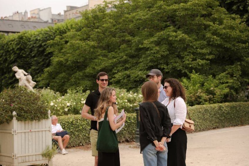 A group of people standing outdoors, a statue, and a hedge. 1