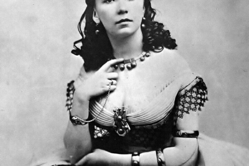 A person in a historical costume with lace details, a brooch, and a chain. 2