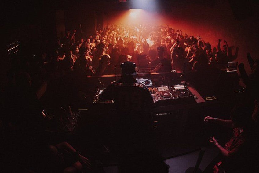 A crowded indoor event with a DJ booth and a stage with bright lights. 1