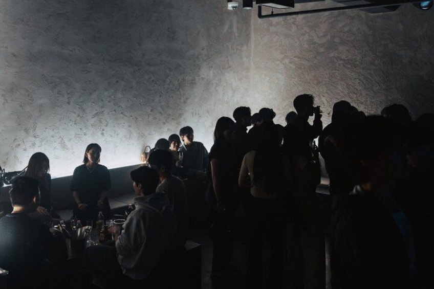 A group of people in a dimly lit room with a textured wall. 4