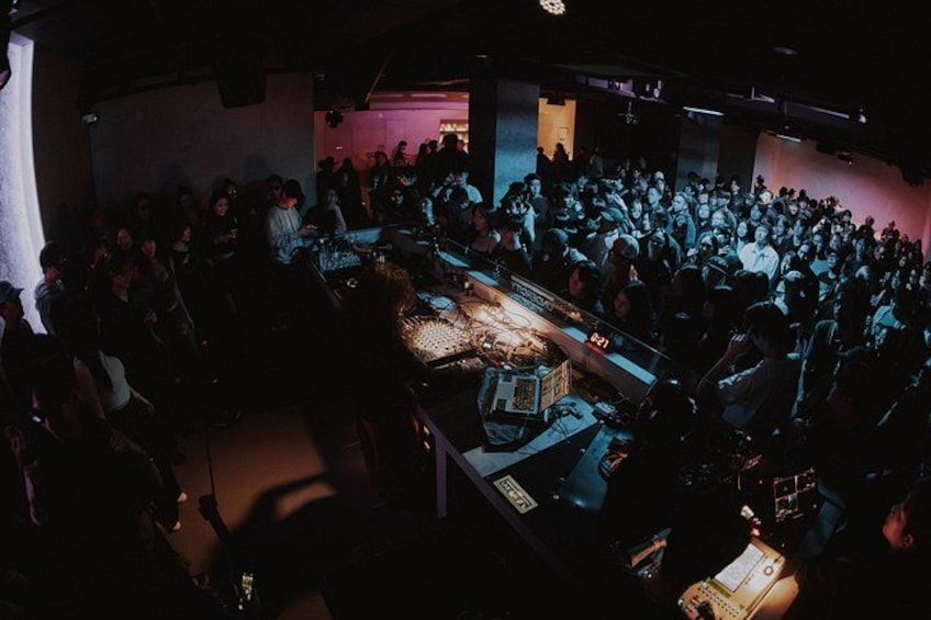 A crowded indoor event with a DJ booth and audience. 2