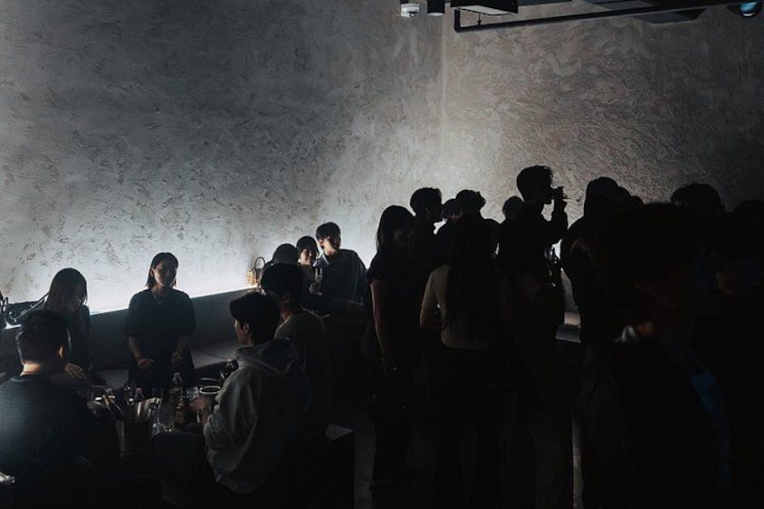 A group of people gathered in a dimly lit room with a textured wall. 3