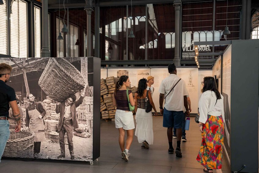 A group of people walking through an exhibition space with a large historical photograph and informational displays. 3