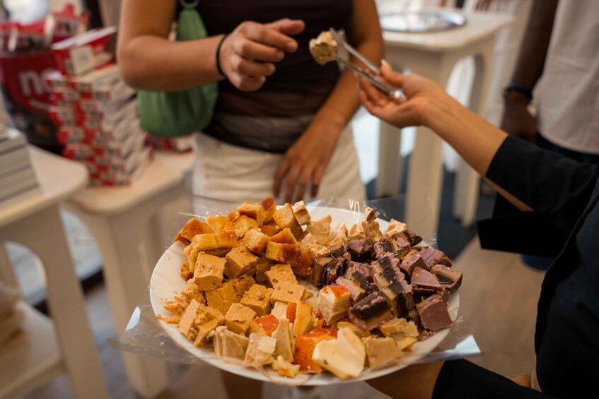 A person holding a plate with various food items, including tofu and meat, in a casual dining setting. 2