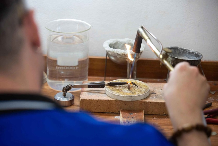 A person conducting a chemistry experiment with a Bunsen burner, a beaker, and a crucible on a wooden table. 1