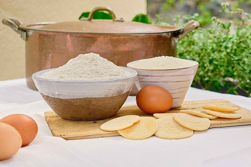 A kitchen setting with a bowl of flour, a bowl of sugar, a brown egg, and a wooden cutting board with cookie dough. 3