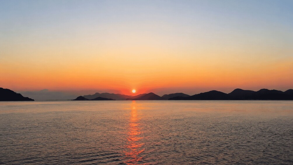 A sunset over a calm sea with distant landforms silhouetted against the sky. 5