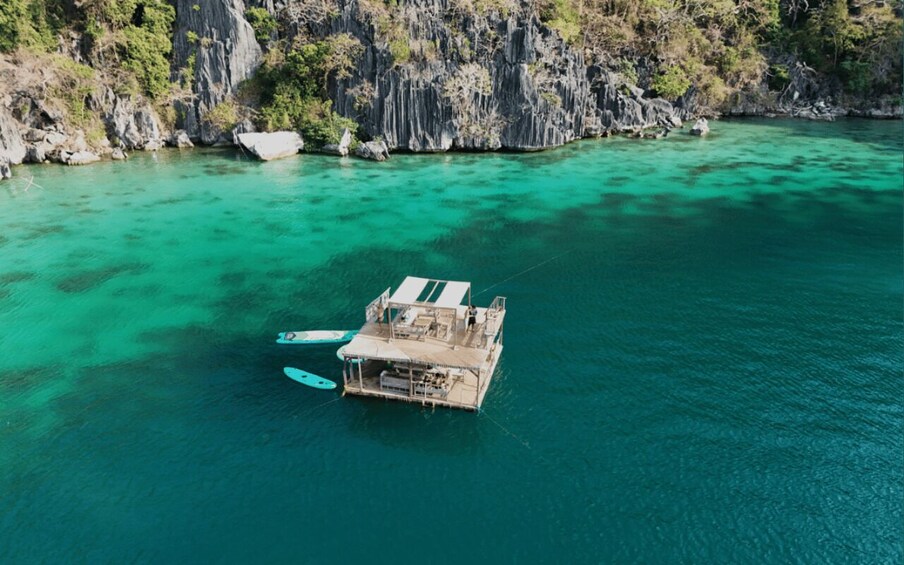 A boat anchored in clear turquoise waters with rocky cliffs in the background. 2